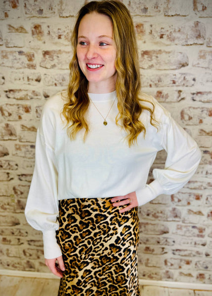 Person wearing a white blouse and leopard print skirt against a brick wall.