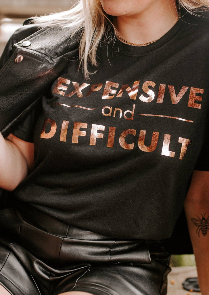 Woman wearing Black T-Shirt that Says Expensive and Difficult with rose gold letters  